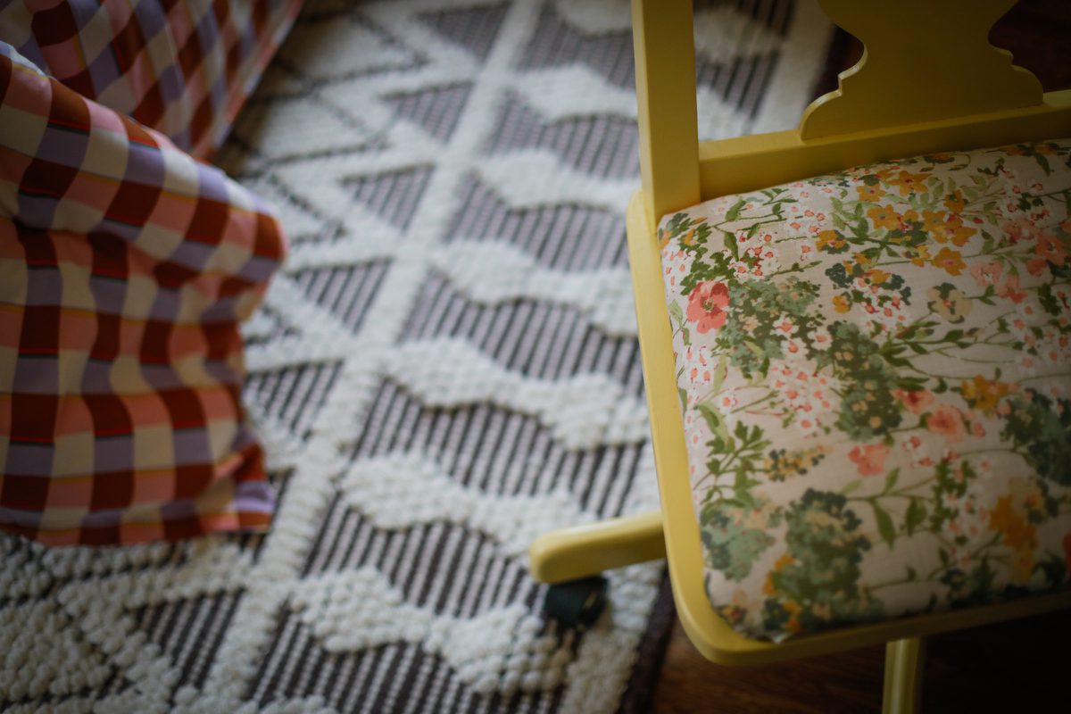 A detail photo of a desk chair with floral fabric, a bed spread and a rung.