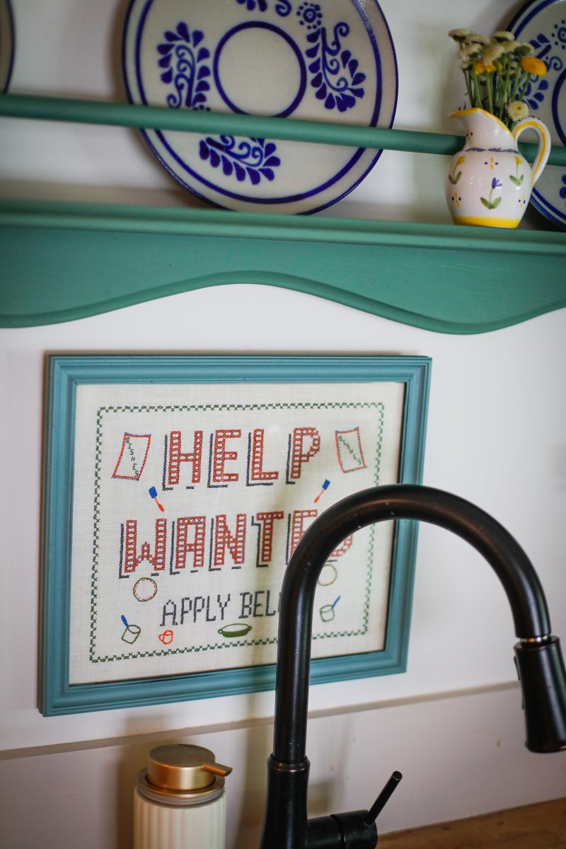 A picture on a wall above a kitchen sink that say Help Wanted.